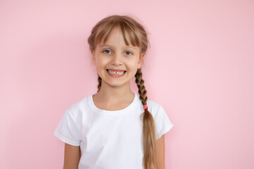 Pretty little girl in a white t-shirt smiling on a pink background