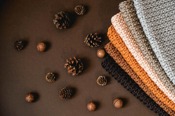 Stack of knitted material from threads of brown, orange, gray colors with pine cones a brown background. Top view. Copy, empty space for text