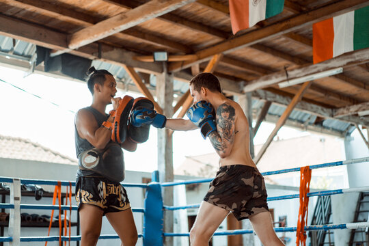 Training in the gym in the ring with a muay thai trainer. Tattooed caucasian man and Asian trainer. Muay thai training.