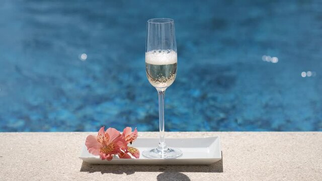 Close up of poured glass with champagne or prosecco on swimming pool or sea background. Full glass with cold champagne with foam and bubbles. Luxury alcohol drink, romantic vacation. Sparkling wine.