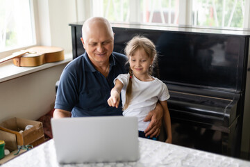 Portrait of grandfather and granddaughter doing homework with laptop.