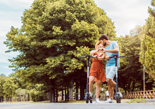 Portrait of couple in love kissing using electric scooter in the park - Millennial people riding new modern ecological service transport.