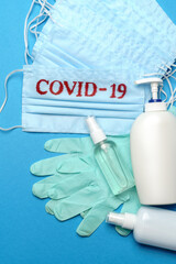 Stack of Disposable blue medical face masks with COVID-19 sign, rubber latex gloves and alcohol hand sanitizer antiseptic on blue background