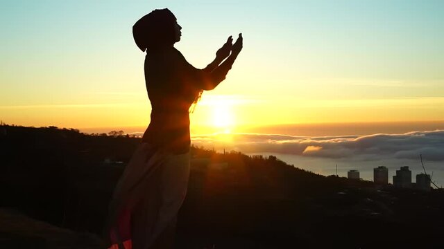Eid al-Adha Islamic holiday. Silhouette of Muslim woman making Dua to Allah outdoor. Beautiful dawn, sunrise