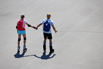 Couple riding on roller skates on a street holding hands, top view. Summer leisure in a city, healthy lifestyle