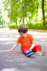 Fototapeta premium A boy draws with crayons on the asphalt . Painting. Summer. Summer games on the street. Children's entertainment and leisure. Chalk for asphalt .
