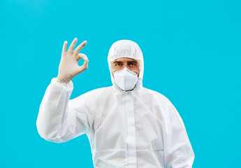 Doctor in protective medical suit showing  ok sign isolated on blue background