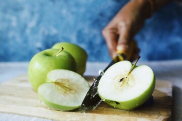 woman hand cutting green apple on chopping board.