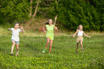 Obraz premium Kids, children running on meadow in summer's sunlight. Look happy, cheerful with sincere bright emotions. Cute caucasian boys and girls. Concept of childhood, happiness, movement, family and summer.