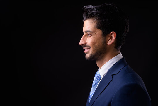 Young handsome bearded Persian businessman against black background