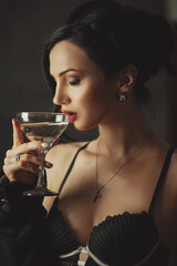 Fashion model in lingerie with wavy hairstyle holding glass of champagne. Attractive young girl with curly hair posing at studio. Face of a beautiful woman with long brown curly hair.