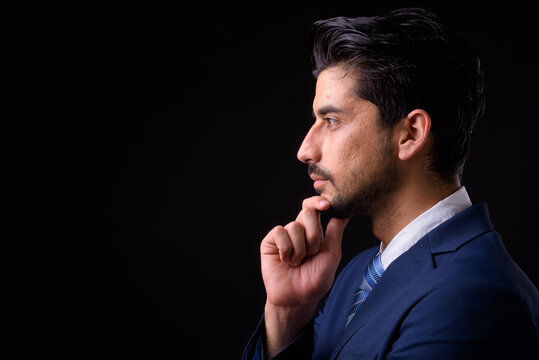 Young handsome bearded Persian businessman against black background