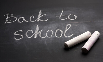 lettering back to school in white chalk on a black school board and a piece of chalk