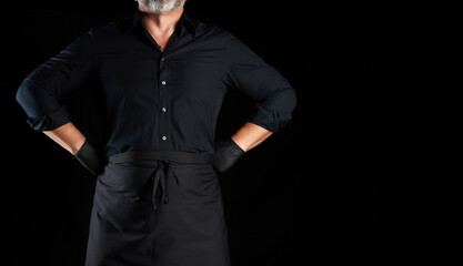 chef in black clothes and latex gloves stands on a black background, hands on hips