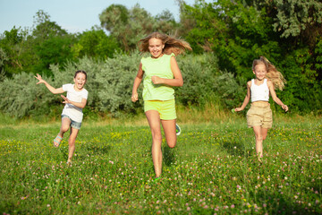 Obraz premium Kids, children running on meadow in summer's sunlight. Look happy, cheerful with sincere bright emotions. Cute caucasian boys and girls. Concept of childhood, happiness, movement, family and summer.