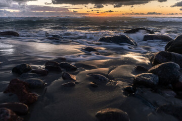 Fototapeta na wymiar long exposure landscape, rocky ocean coastline with blurry waves in orange sunset light