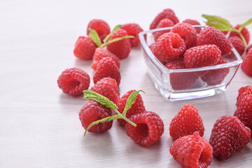 Bowl of fresh raspberries with green leaves on wooden background. Front view