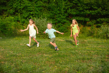 Naklejka premium Kids, children running on meadow in summer's sunlight. Look happy, cheerful with sincere bright emotions. Cute caucasian boys and girls. Concept of childhood, happiness, movement, family and summer.