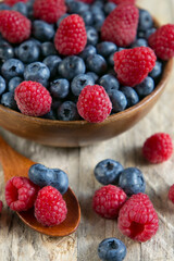 Blueberries and raspberries in a wooden bowl on a wooden table.