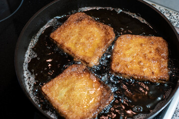 Three pieces of egg bread cooking in hot oil in a pan close up shot