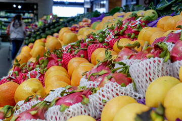 Fruit shop greengrocer display shelf with exotic fruits - mangooes, dragonfruits, oranges, avocadoes.