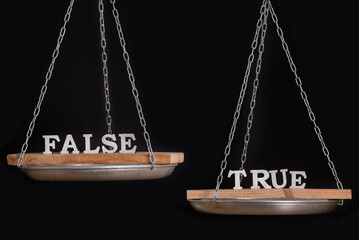 Words truth and false on scales. Disbalance. Black background close up