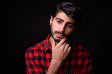 Young handsome bearded Persian man against black background