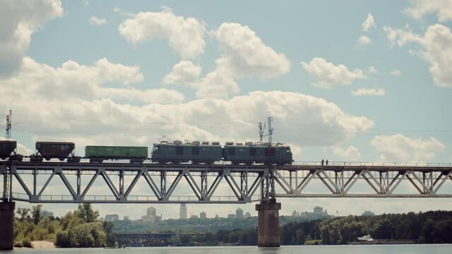 Cargo Train Moving On Railroad Bridge.Kiev City Bridge.Freight Train Passing Through Dnieper River.Electric Locomotive With Wagons Rides On Steel Railway.Heavy Industry Transportation Concept.