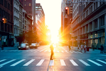 Blurred image of a man walking across the street in New York City with the bright light of sunset shining through the buildings - Powered by Adobe