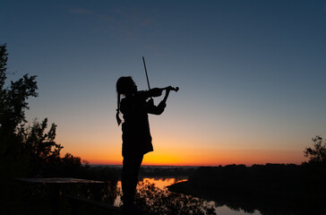 Fototapeta na wymiar Silhouette of a teenage girl with a violin on a background of blue sky in natural light