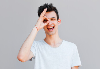 Young handsome man doing ok gesture with hand smiling, eye looking through fingers with happy face.