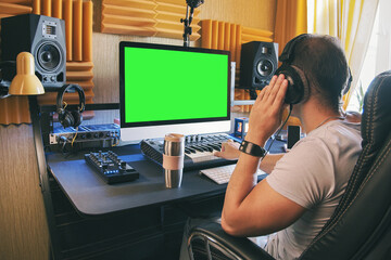 A man produce electronic music in home studio using headphones and look in green screen on monitor - Powered by Adobe