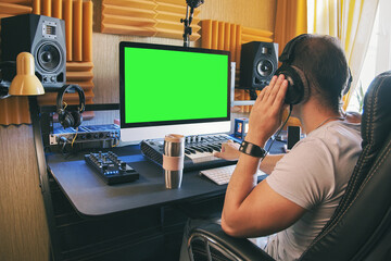 A man produce electronic music in home studio using headphones and look in green screen on monitor