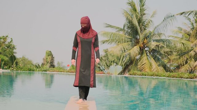 Muslim woman in swimsuit walking on water of swimming pool outdoors.