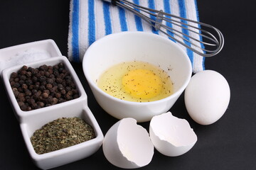 Broken chicken egg sasoned with black pepper. Its ready to be whisked by whisker. Its kept on black background with blue stripped napkin.