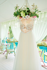Beautiful wedding dress hanging on hanger on chandelier on hotel terrace, copy space. Bridal morning preparations