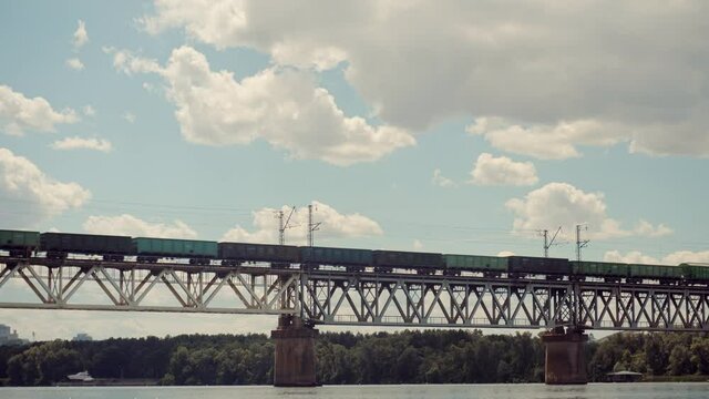 Cargo Train Moving On Railroad Bridge.Kiev City Bridge.Freight Train Passing Through Dnieper River.Electric Locomotive With Wagons Rides On Steel Railway.Heavy Industry Transportation Concept.