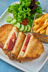 Grilled and pressed toast with turkish sausage, cheese, tomato and lettuce served on white plate.