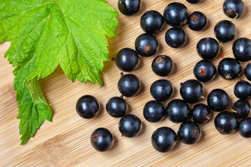 Fresh ripe black currants heap on wooden background. Natural organic berries with green leaves scattered on weathered wooden table, new berry harvest. Top view