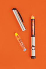 Insulin Pen on orange background, close-up, flat lay. Diabetes control concept