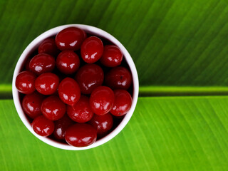 Red color cherry fruits in a white bowl against green background, with copy space, caption