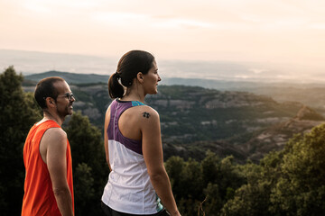 Trail running couple looking out at landscape in the sunset.