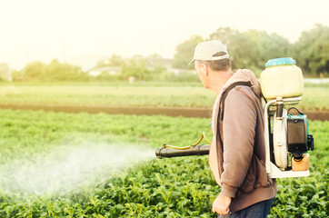 Fototapeta premium A farmer with a mist sprayer spray treats the potato plantation from pests and fungus infection. Agriculture and agribusiness. Harvest processing. Protection and care. Use chemicals in agriculture.