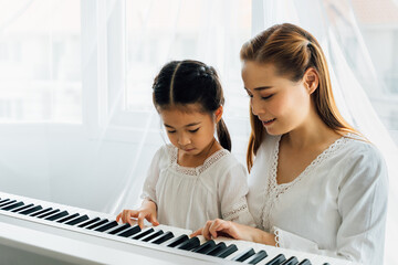 Chinese mother watching young daughter play keyboard