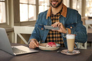 Young blogger taking picture of dessert at table in cafe, closeup