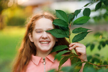 Laughing girl holding a branch with green leaves near her face.