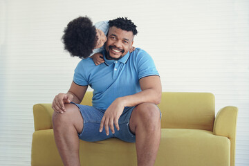 An African American family father and little son playing together. Kid boy kissing his dad on sofa at home