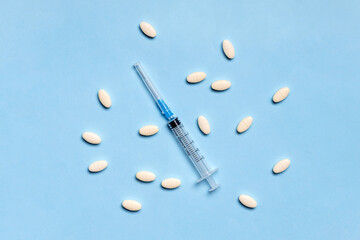 Medical syringe with pills on blue background. Injectable drugs, vaccination concept.