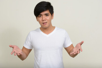 Portrait of young handsome Asian man against white background