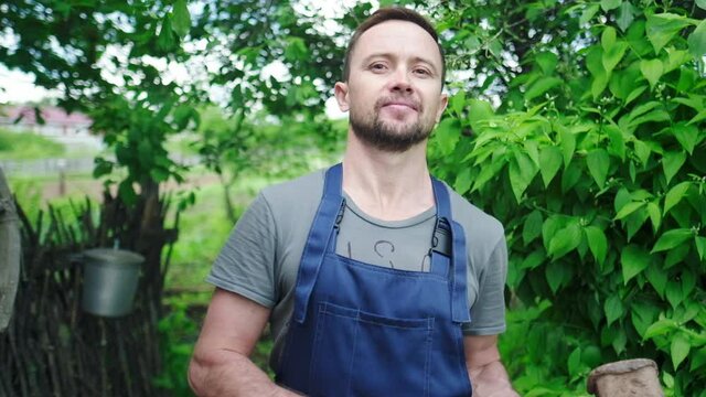 Playful worker in the garden. Young adult man plays with heavy hammer in the garden and looks at the camera
